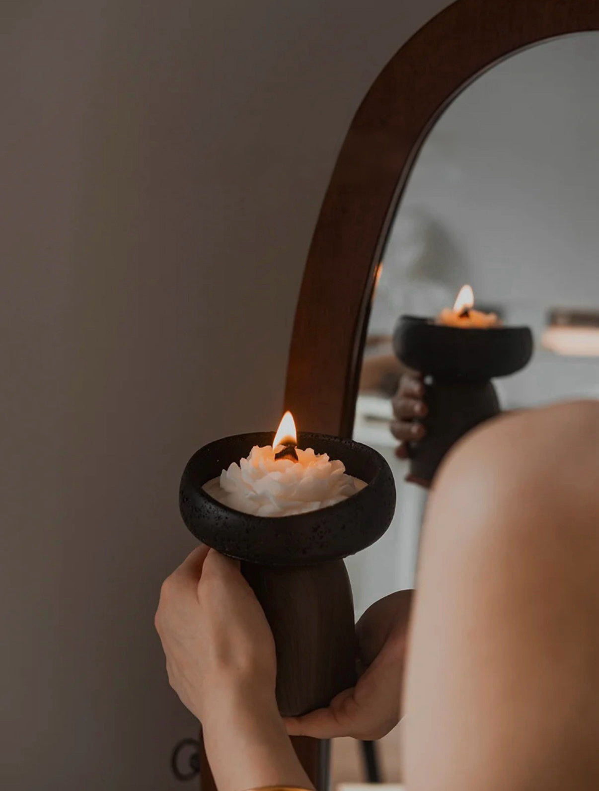 Person holding a lit candle in a decorative holder in front of a mirror.