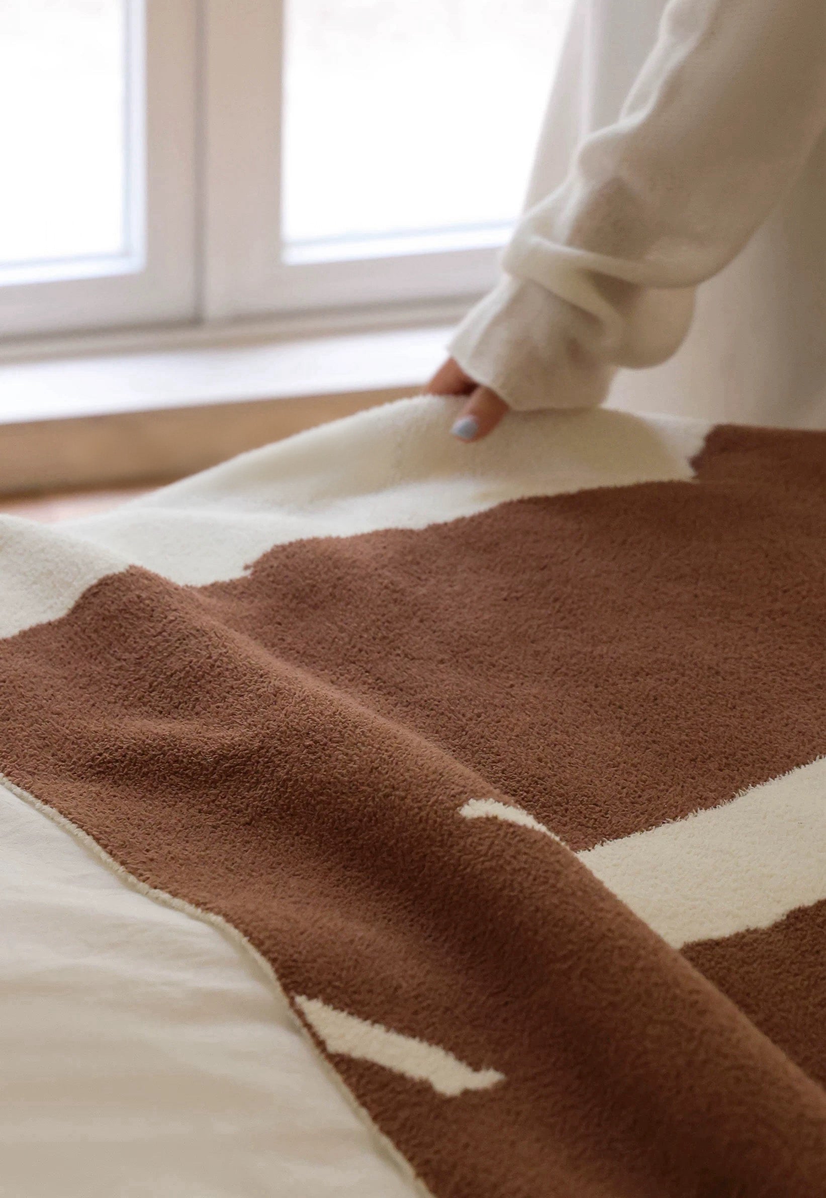 Brown and beige patterned blanket on a bed with a person partially visible.
