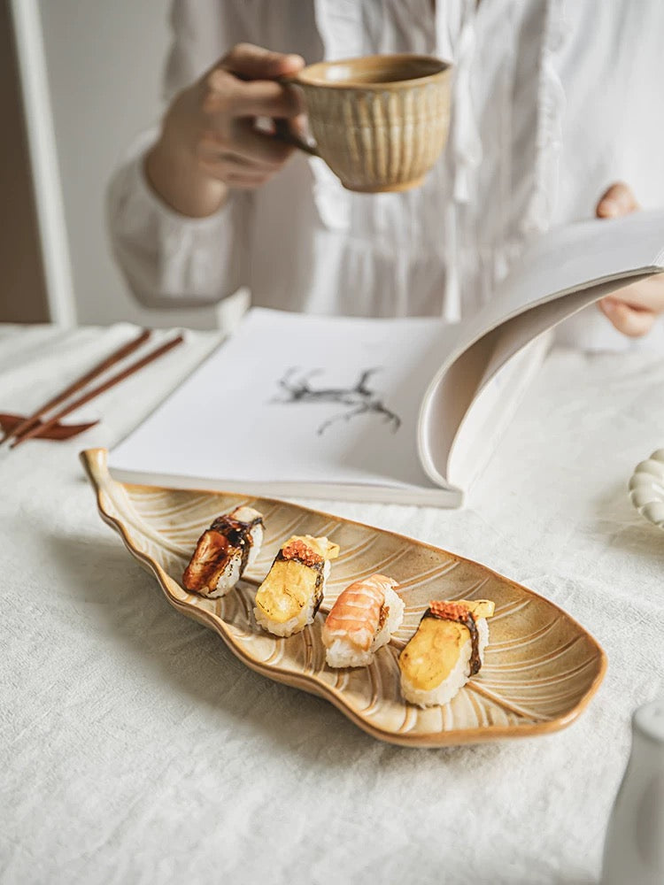 Person holding a cup with a leaf-shaped plate of sushi on a light surface