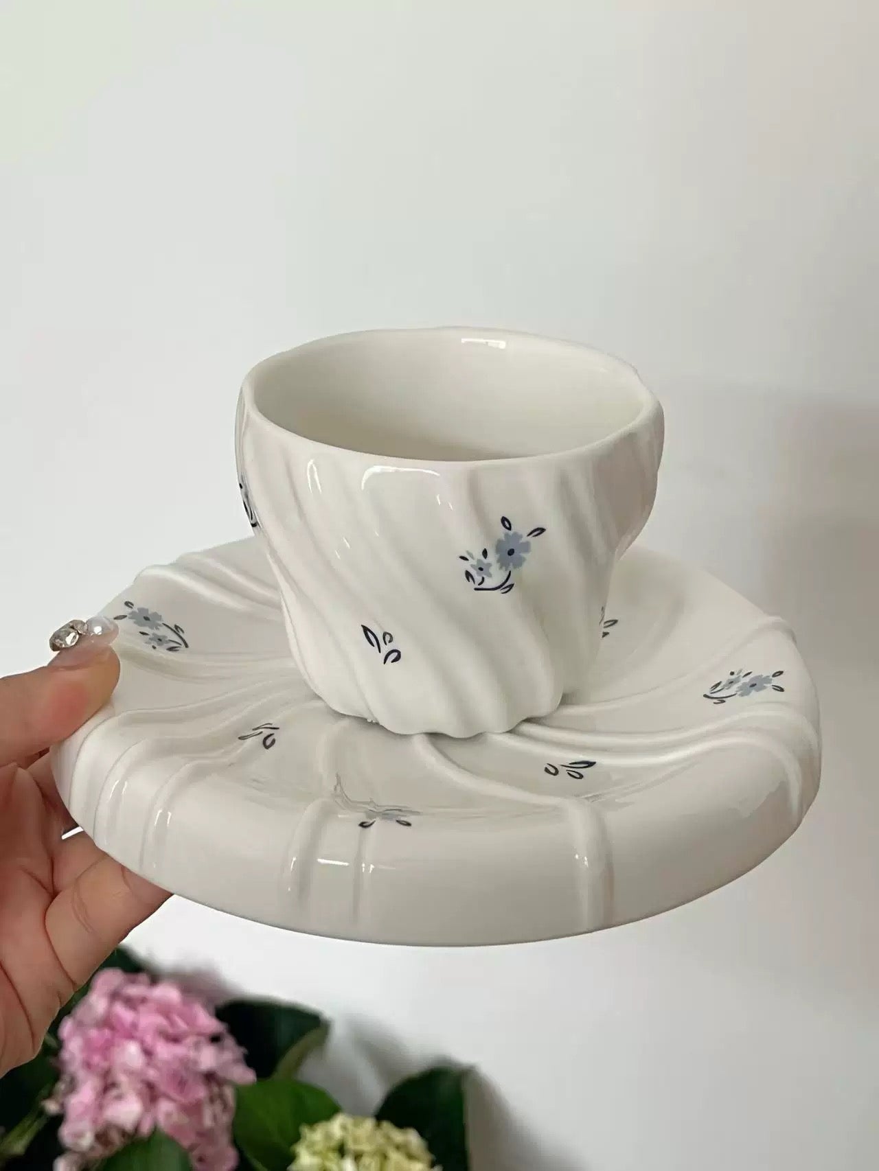 Ceramic cup and saucer with floral design held against a white background