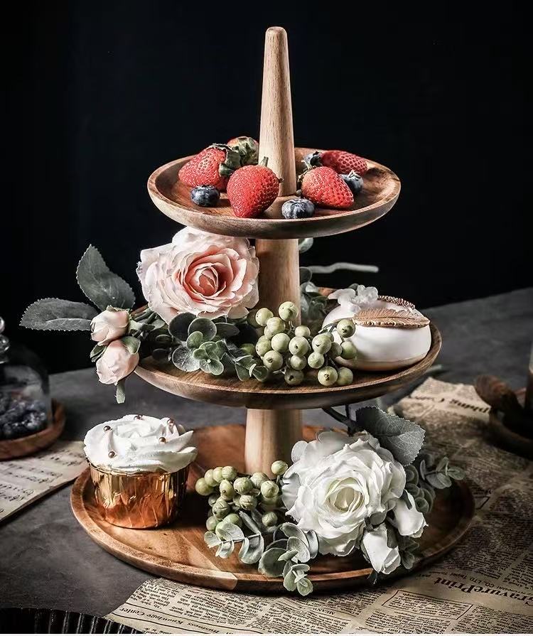 Three-tiered wooden serving tray with fruits, flowers, and a candle on a dark background