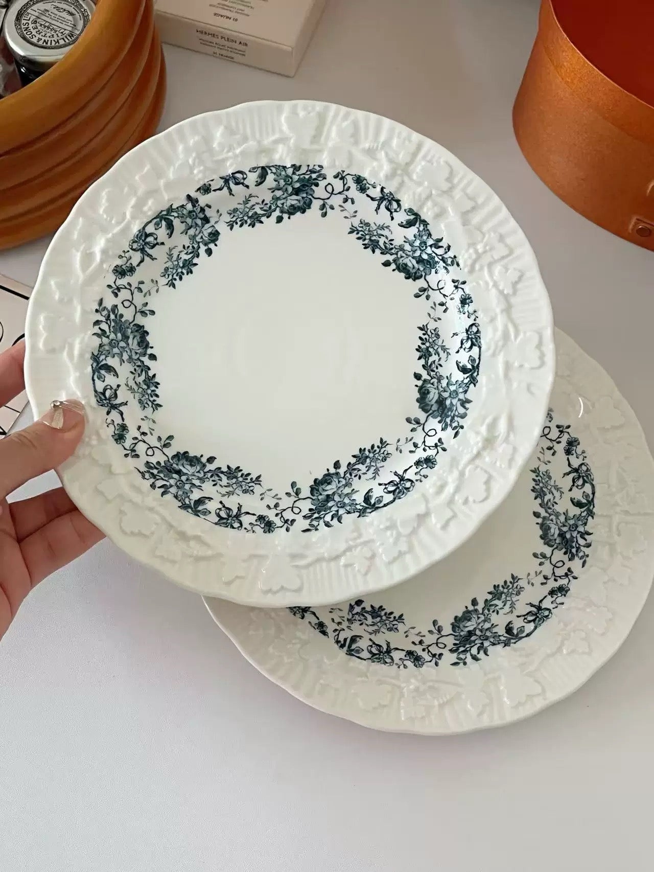 White plates with blue floral patterns held by a hand on a white surface.