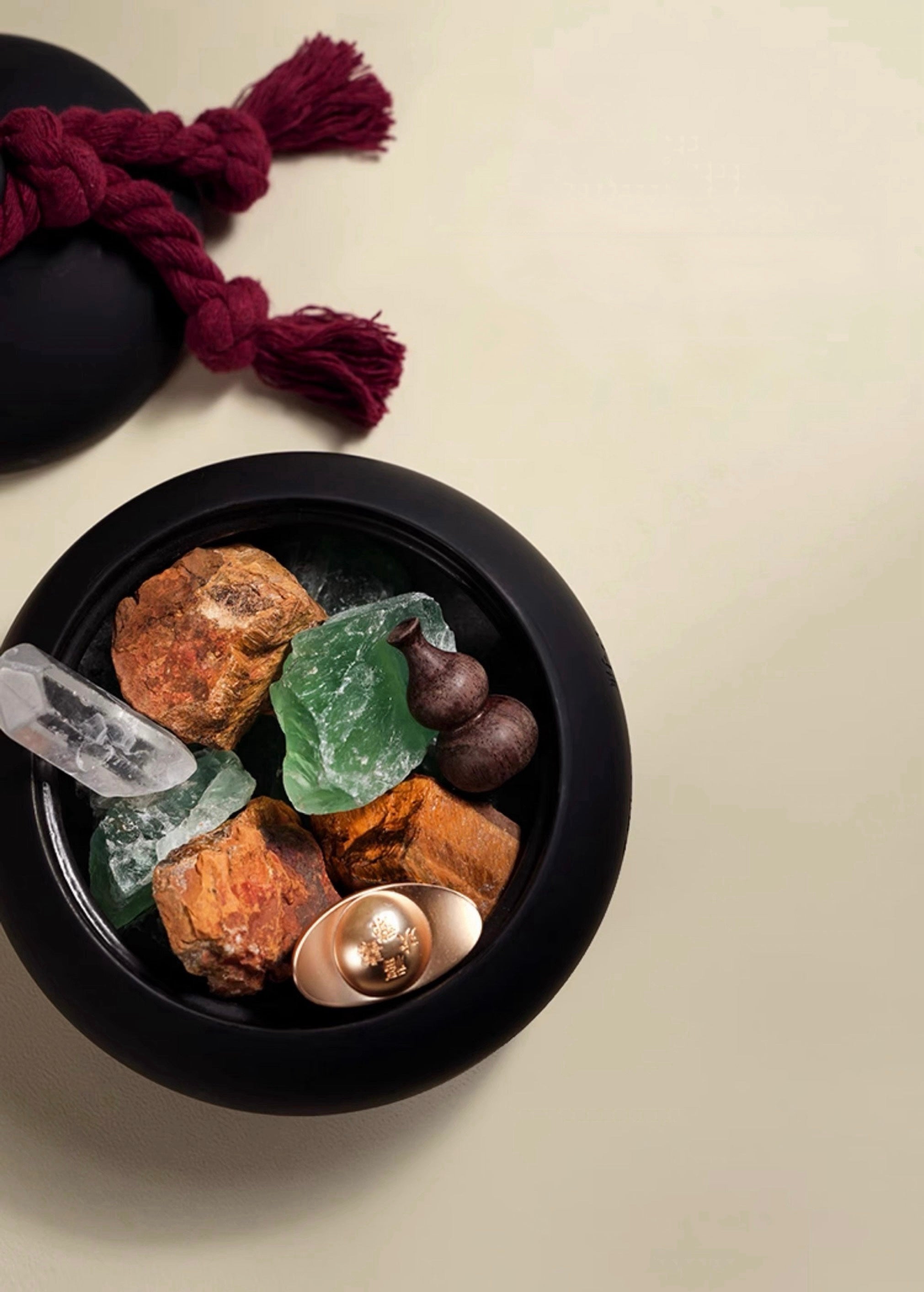 Black bowl with rocks, crystals, and a spoon on a beige background