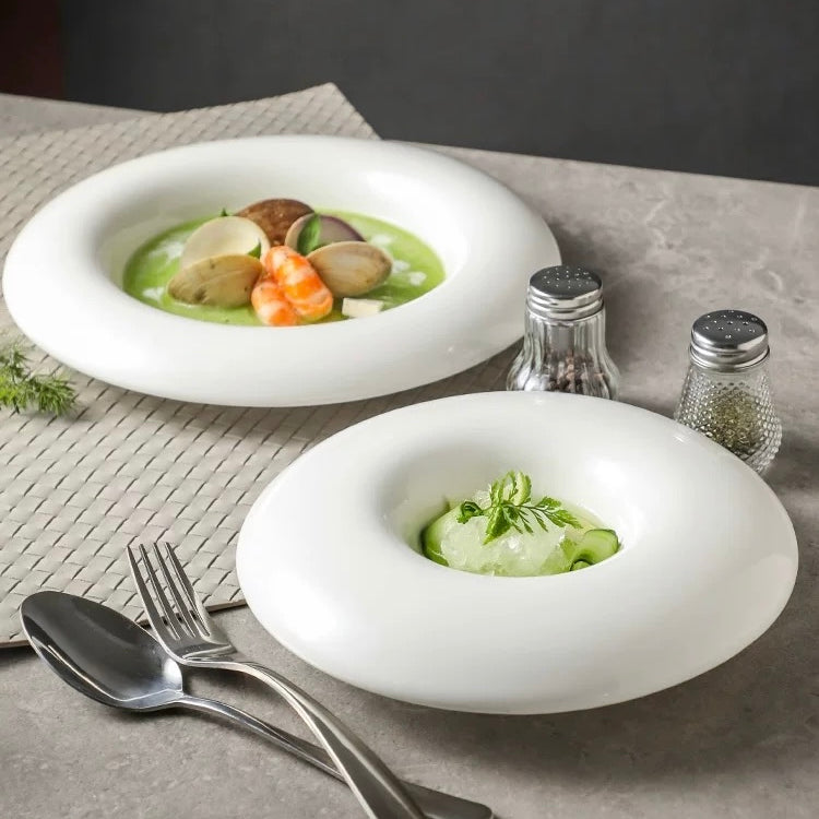 Two white bowls with green soup and garnishes on a gray surface with silverware and saltshakers.