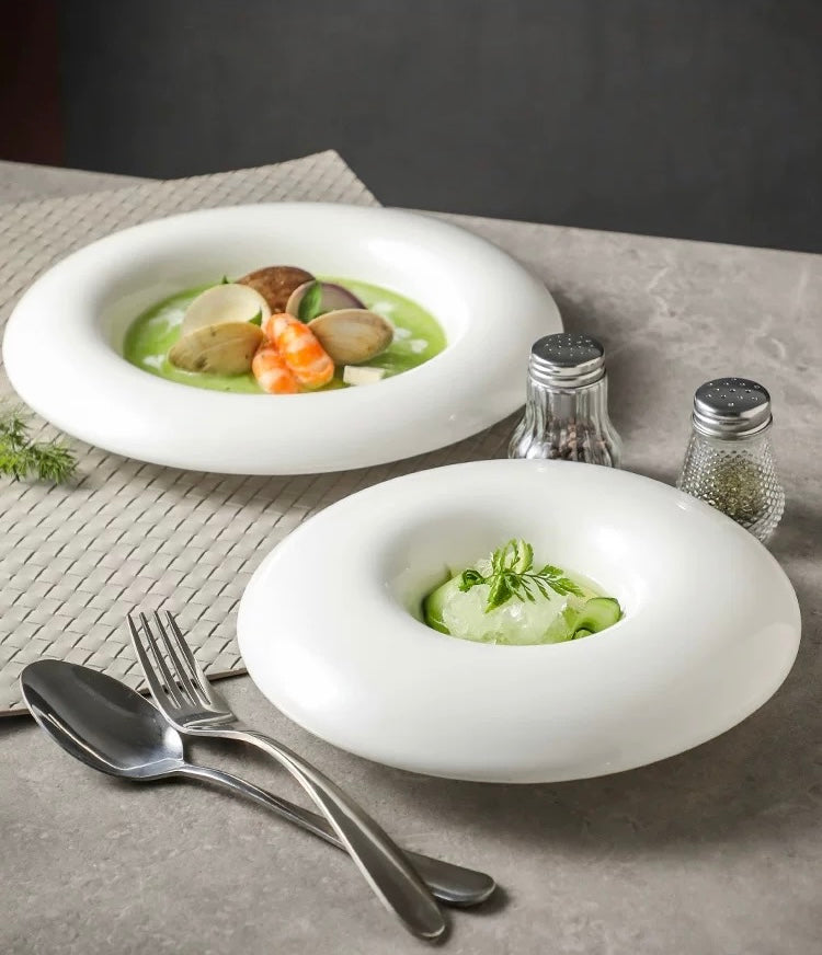 Two white bowls with green soup and garnishes on a gray surface with silverware and saltshakers.