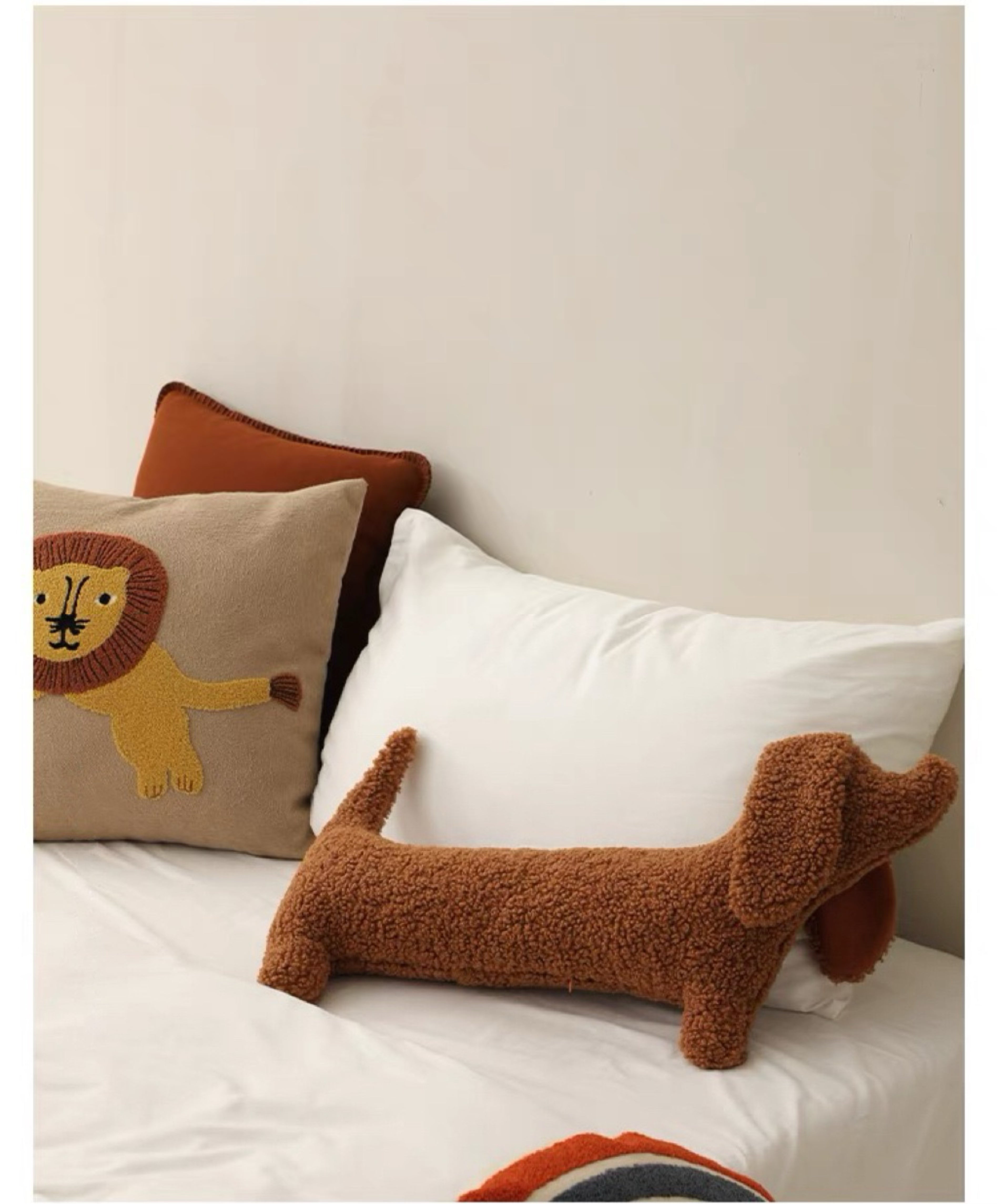 A brown dog-shaped cushion pillow on a bed, with other pillows and bedding in the background.