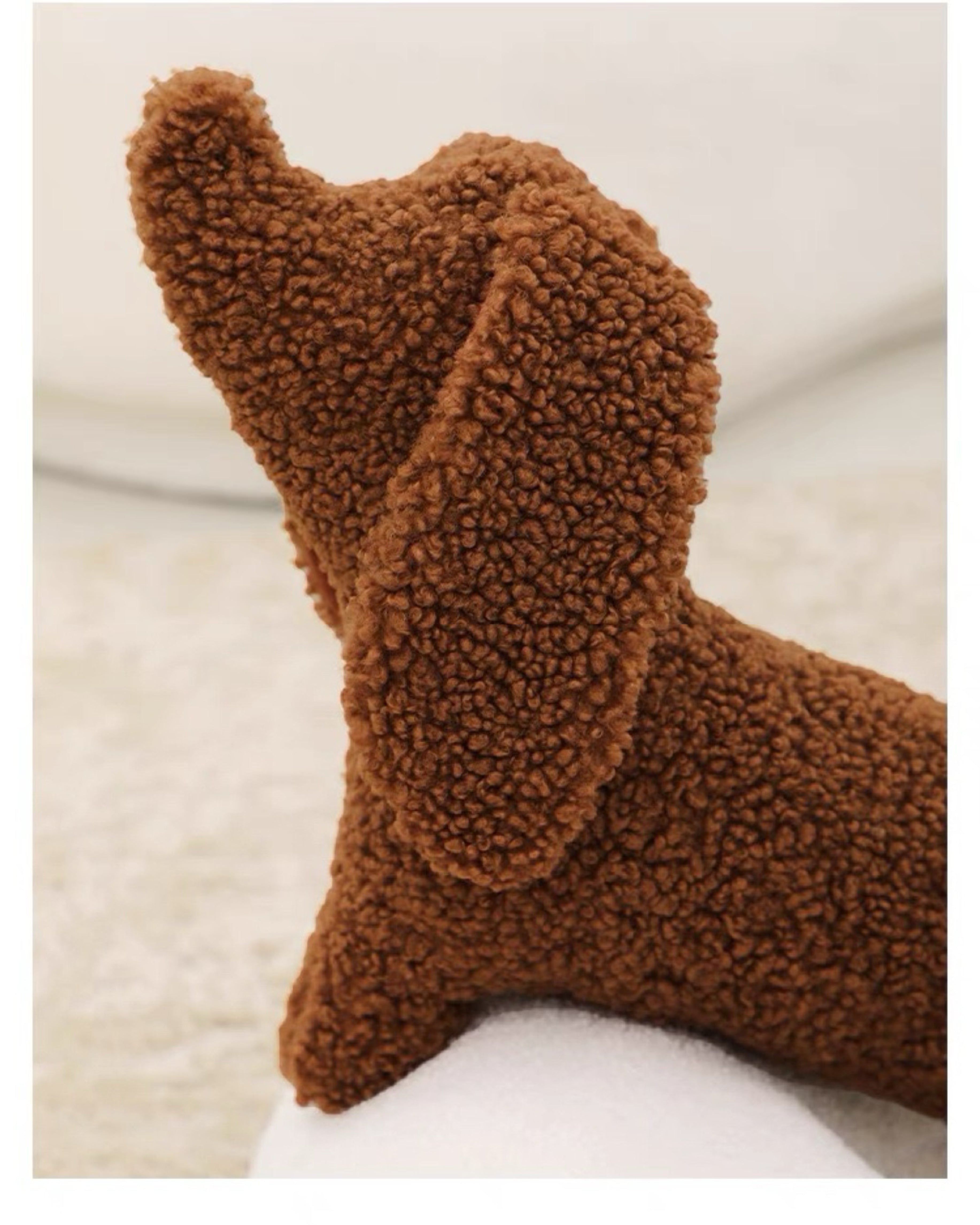 A brown dog-shaped cushion pillow on a bed, with other pillows and bedding in the background.