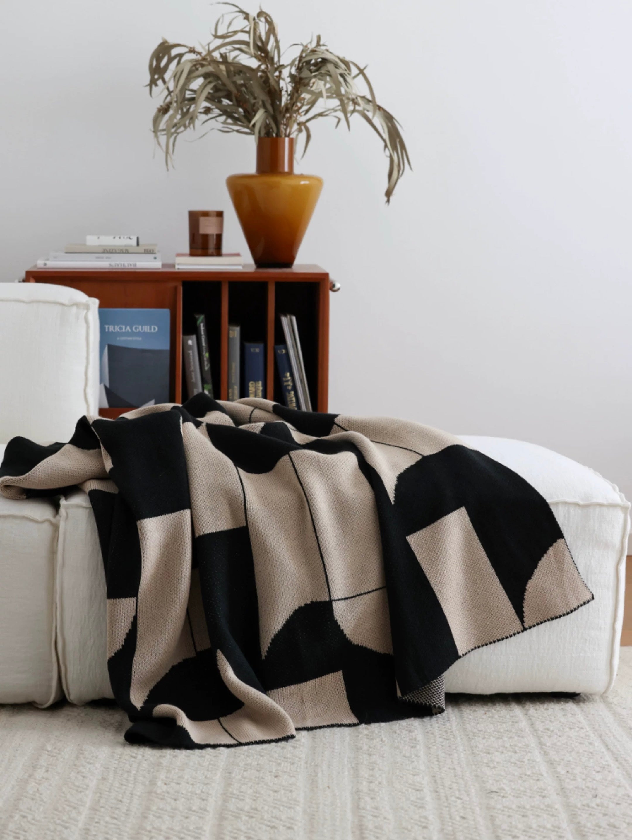 Black and beige patterned blanket draped over a white sofa with a wooden side table and plant in the background.