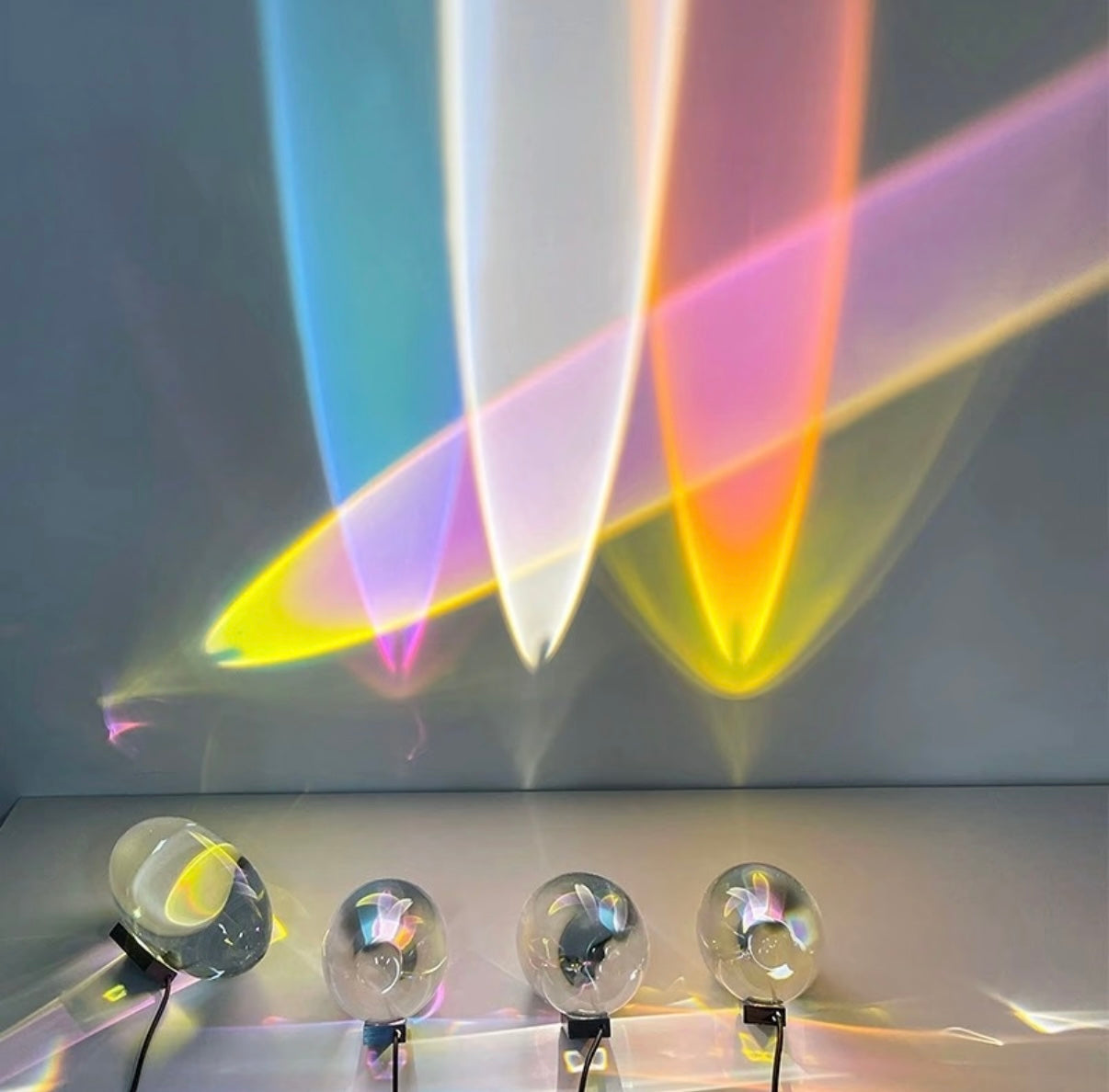 Colorful light beams projected onto a wall with four clear spherical objects below.