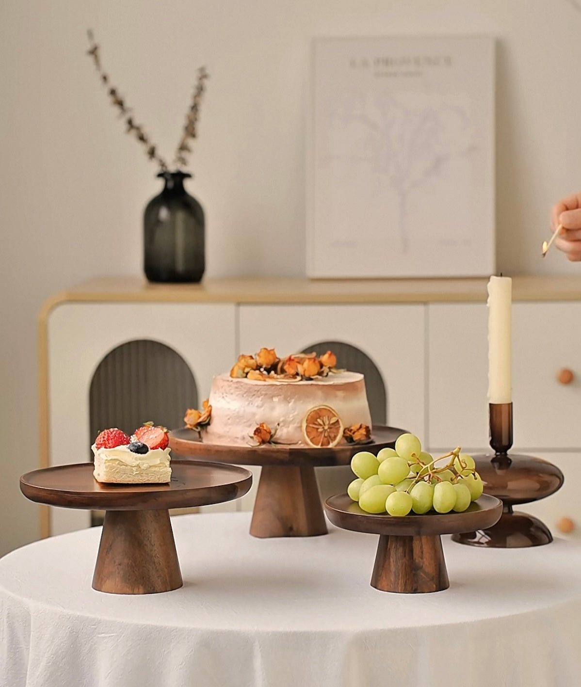 Wooden cake stands with small cakes and fruits on a table.