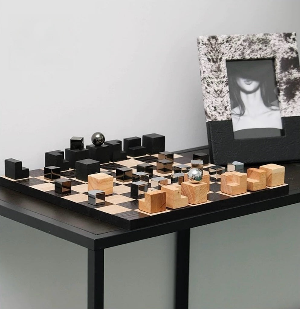 Modern chess set with black and wood pieces on a table against a plain wall.