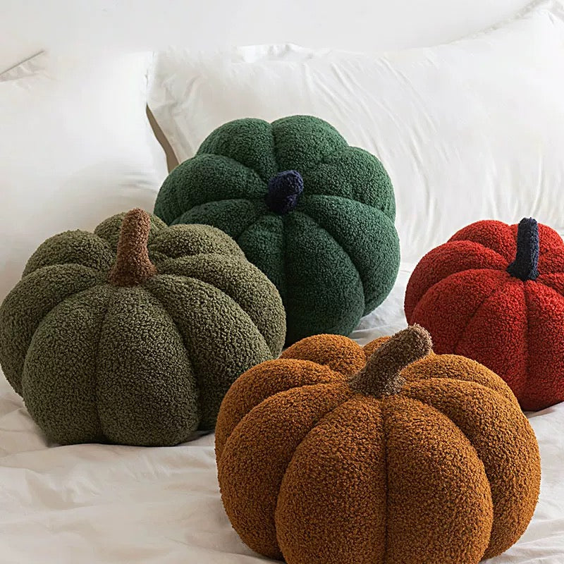 Four textured pumpkin-shaped cushions in green, red, and brown on a white surface.
