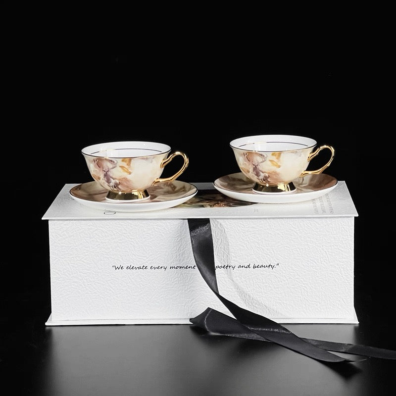 Two marble-patterned teacups with gold accents on a white box with a black ribbon.