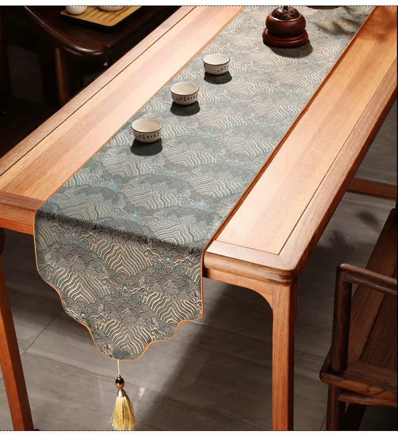 Wooden table with a decorative table runner and small cups on a wooden floor.