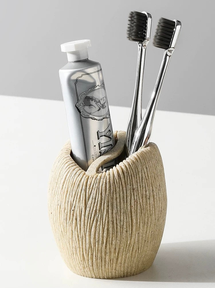 Beige ceramic holder with toothbrushes and a bottle on a white surface