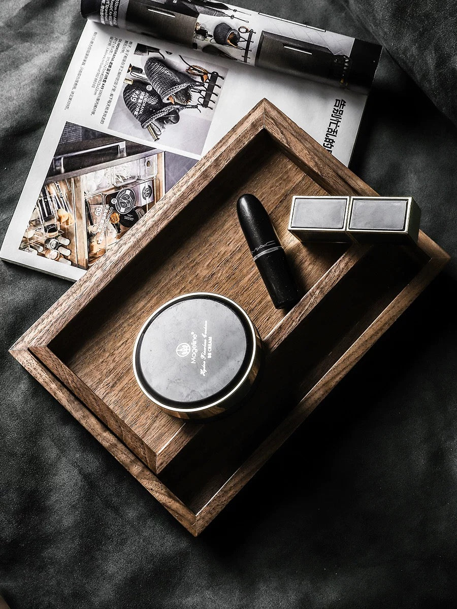 Wooden tray with cosmetic items including a compact mirror, lipstick, and small box on a dark fabric background.