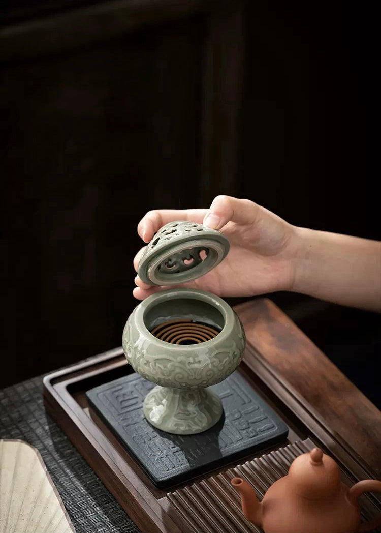 Person holding a ceramic incense burner on a wooden table with a dark background
