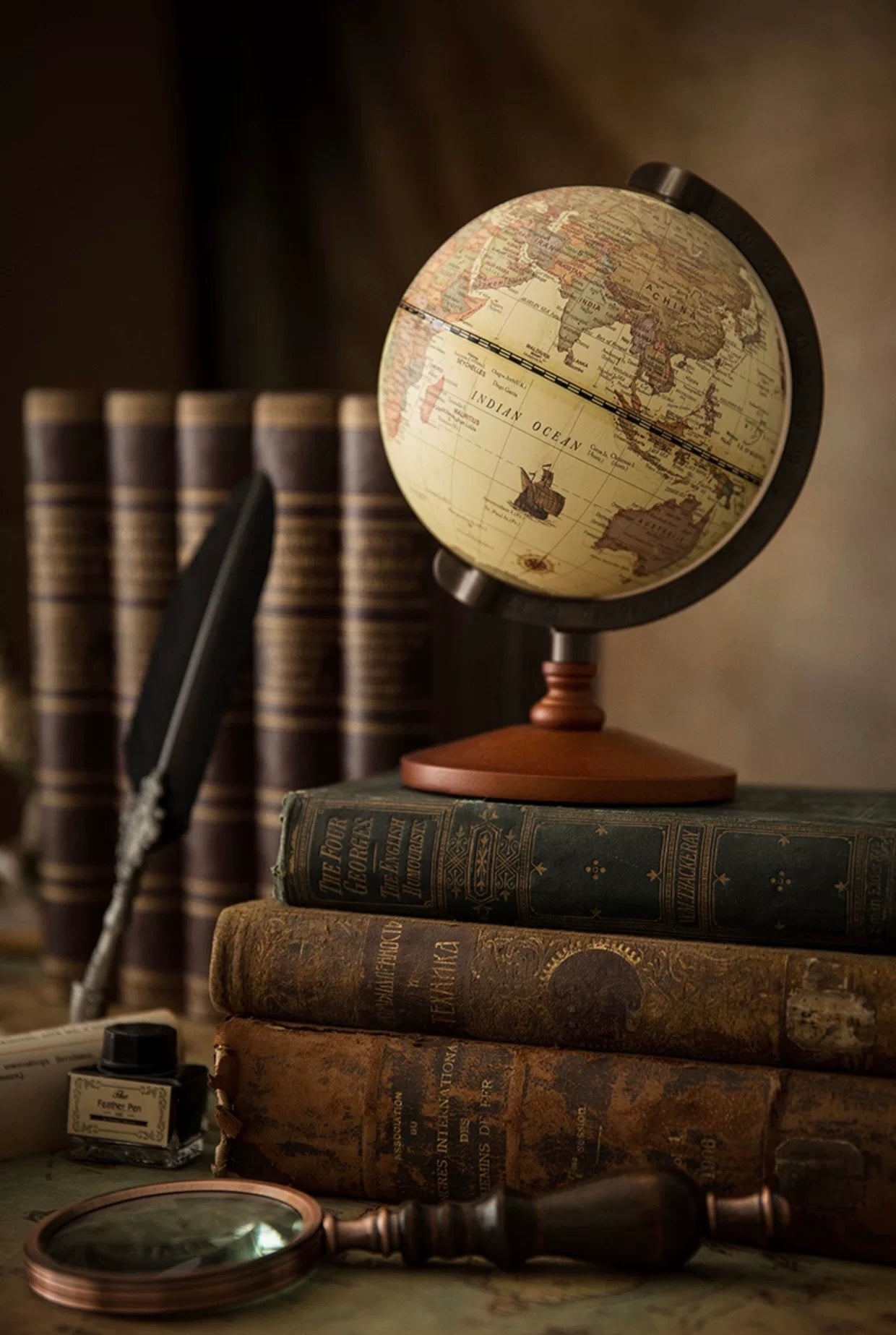 Vintage globe on a stack of old books with a feather quill and inkwell in the background.