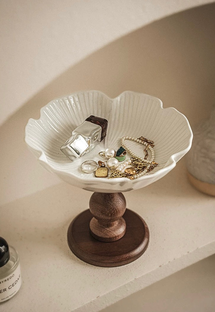 White jewelry dish with wooden base holding jewelry on a neutral background