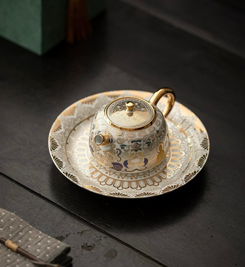 Decorative teapot and saucer set with intricate designs on a dark surface