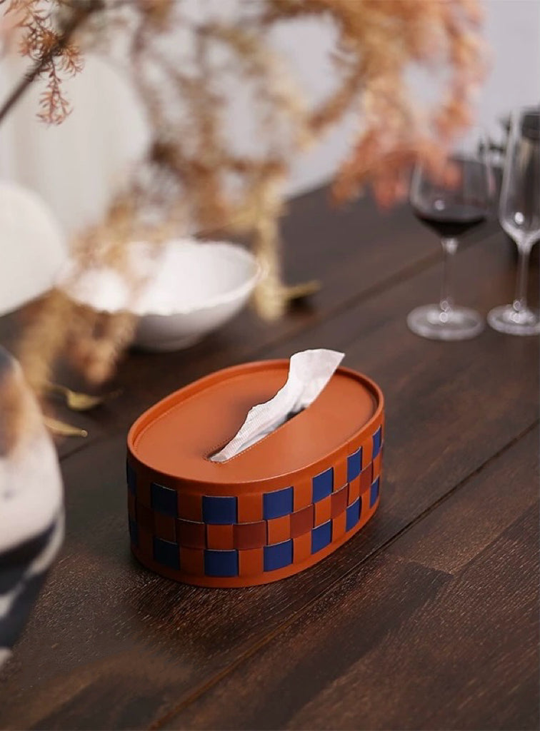 Tissue box with checkered design on a wooden table with wine glasses and decorative elements.