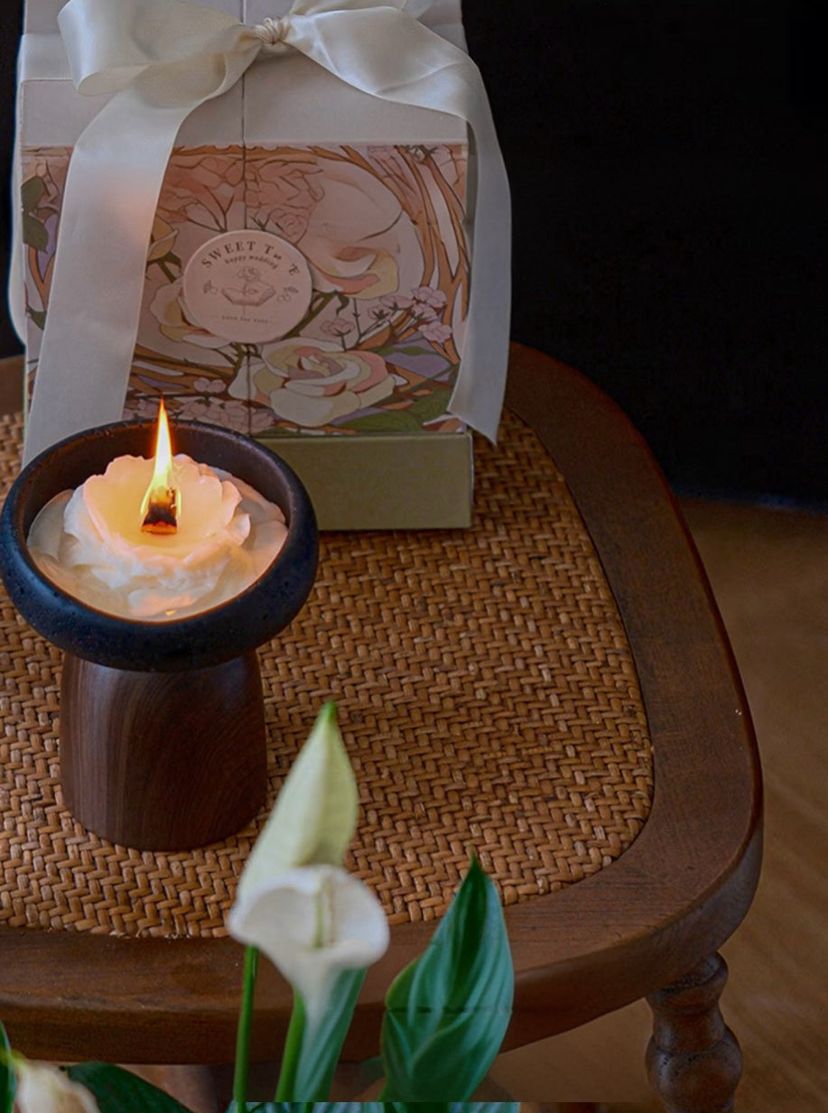 Candle in a wooden holder with a decorative box in the background on a woven mat.