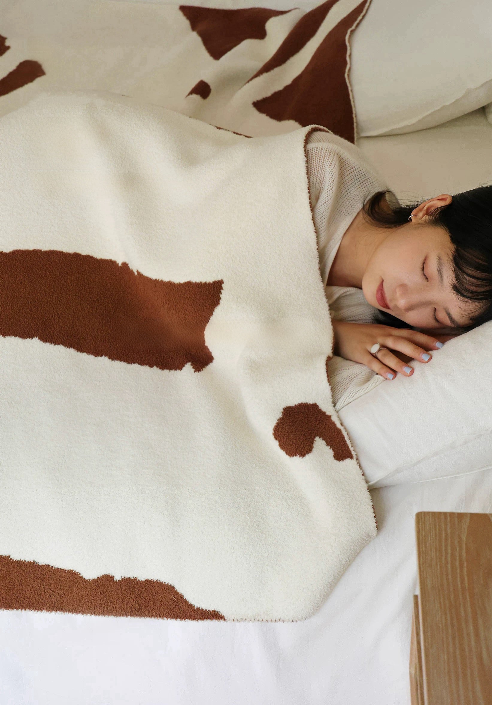 Person lying on a bed with a cow print blanket