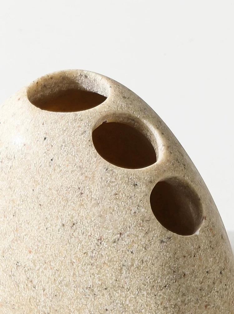 Close-up of a beige ceramic vase with three circular holes on a light gray background