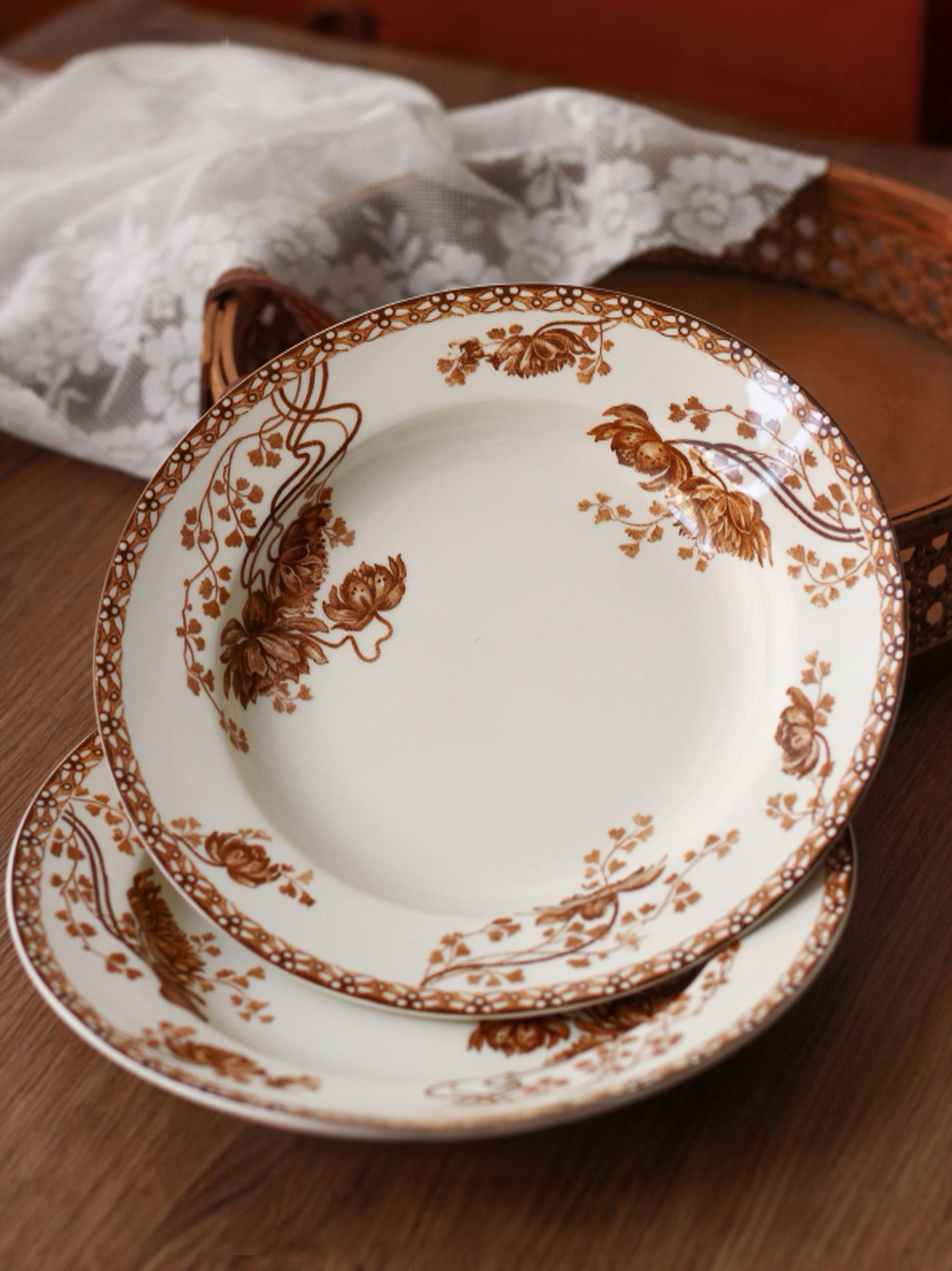 Set of white plates with brown floral patterns on a wooden surface.