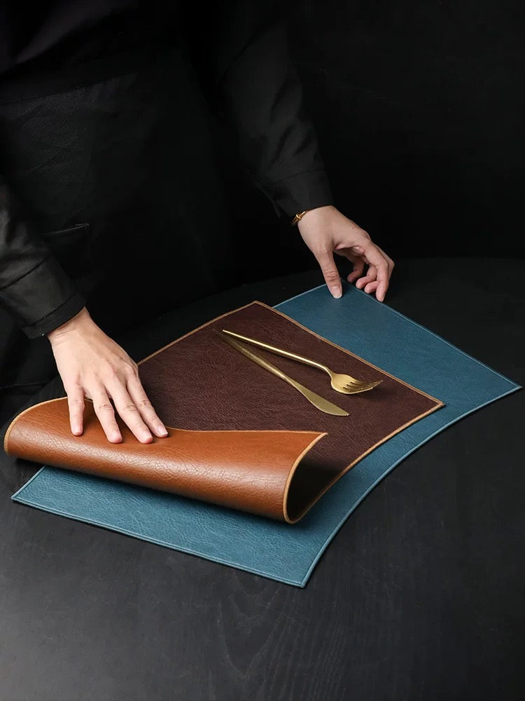 Person unrolling a brown leather placemat with cutlery on a dark surface