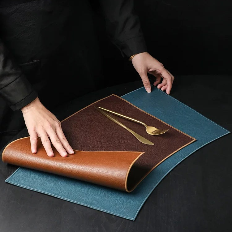 Person unrolling a brown leather placemat with cutlery on a dark surface