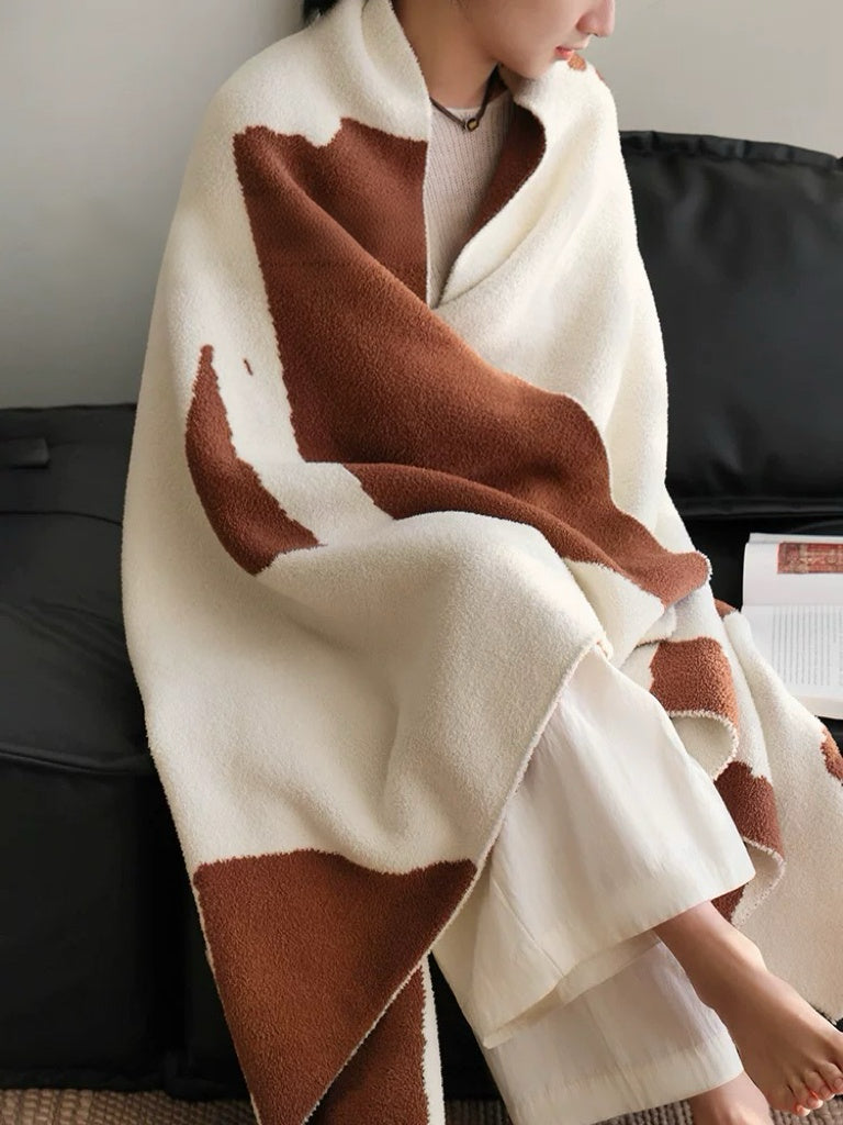 Person wrapped in a brown and white patterned blanket sitting on a couch.