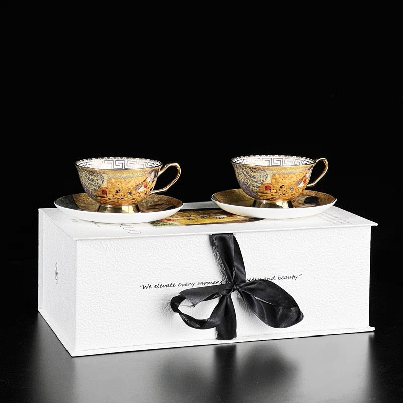 Two ornate teacups and saucers in a white box with a black ribbon on a black background