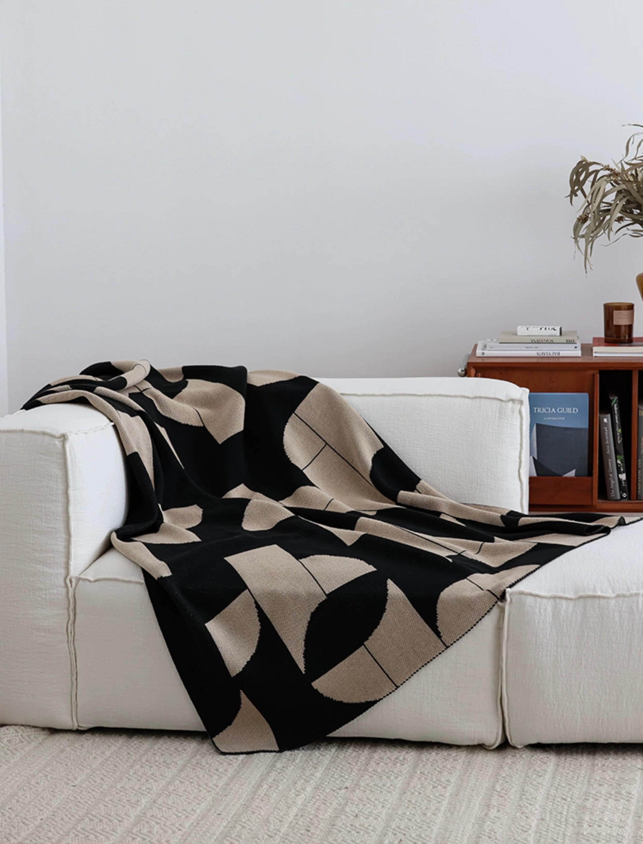 Black and beige patterned blanket draped over a white sofa in a living room setting.