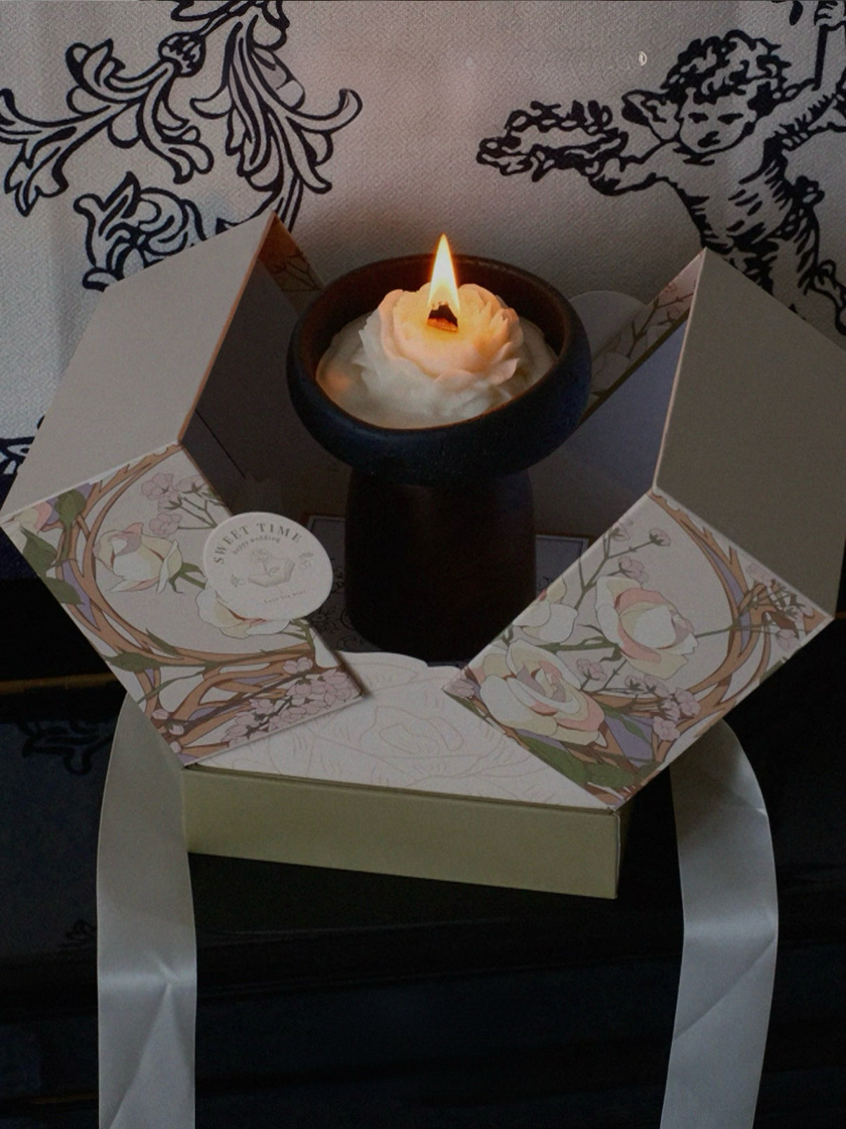 Candle in a decorative box with floral design on a dark background