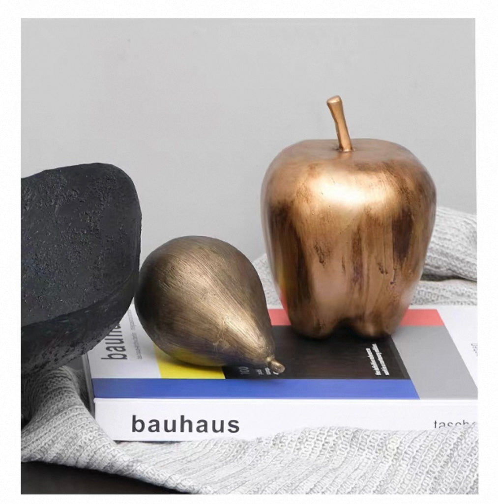 Decorative objects including a bronze apple and pear on a 'Bauhaus' book with a gray background