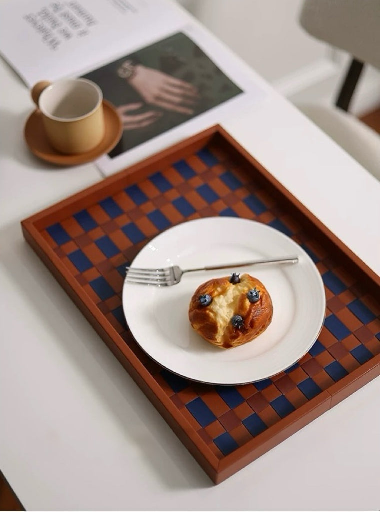 Wooden checkered tray with a plate of food and a cup on a white surface.