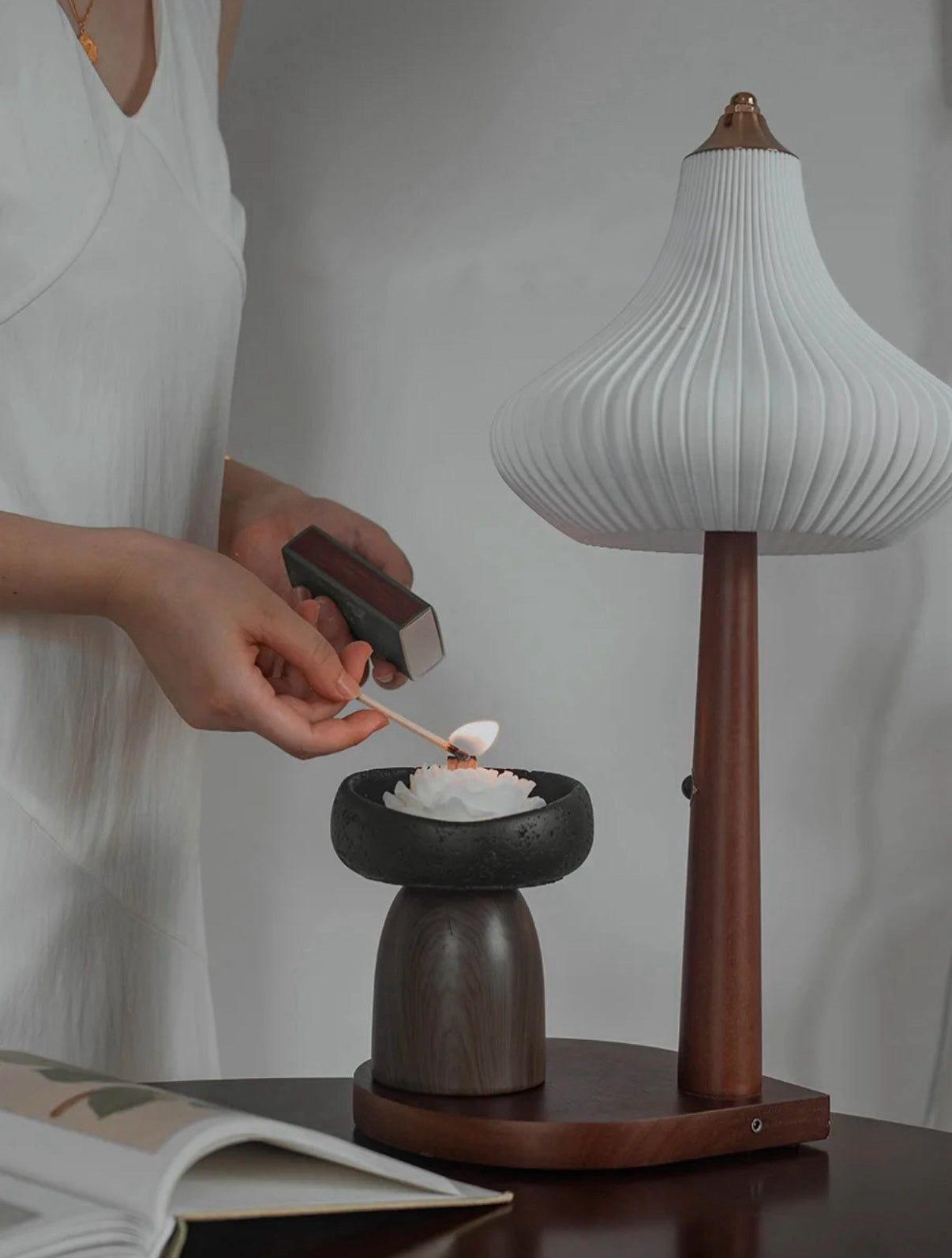 Person lighting a candle in a wooden holder with a modern lamp in the background