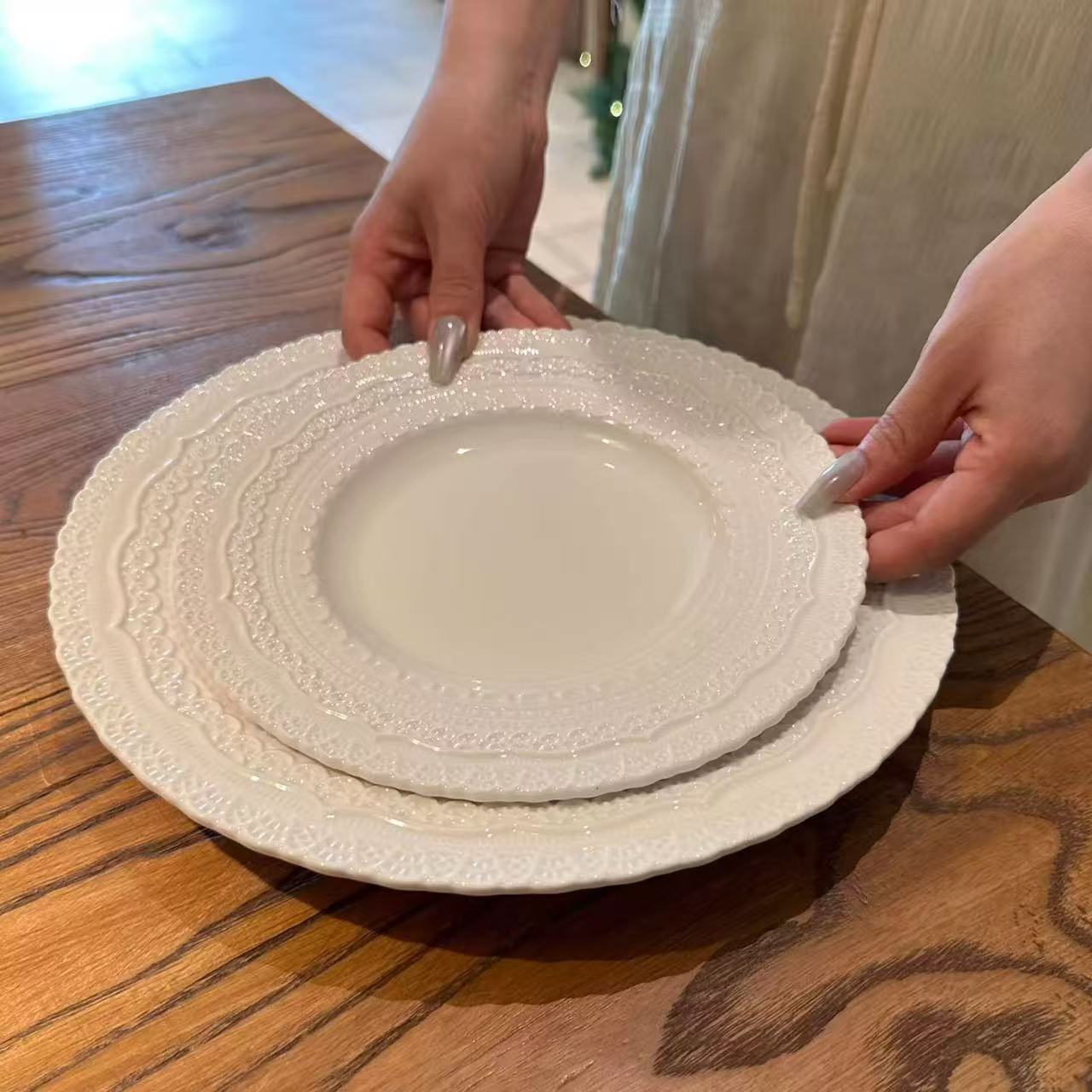 Two hands holding a stack of white ceramic plates on a wooden table.