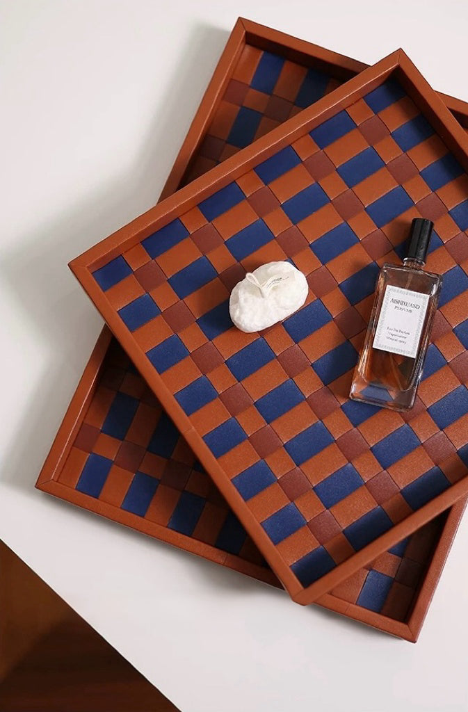 Two wooden trays with a checkered pattern, one with a bottle and a bar of soap on a white surface.