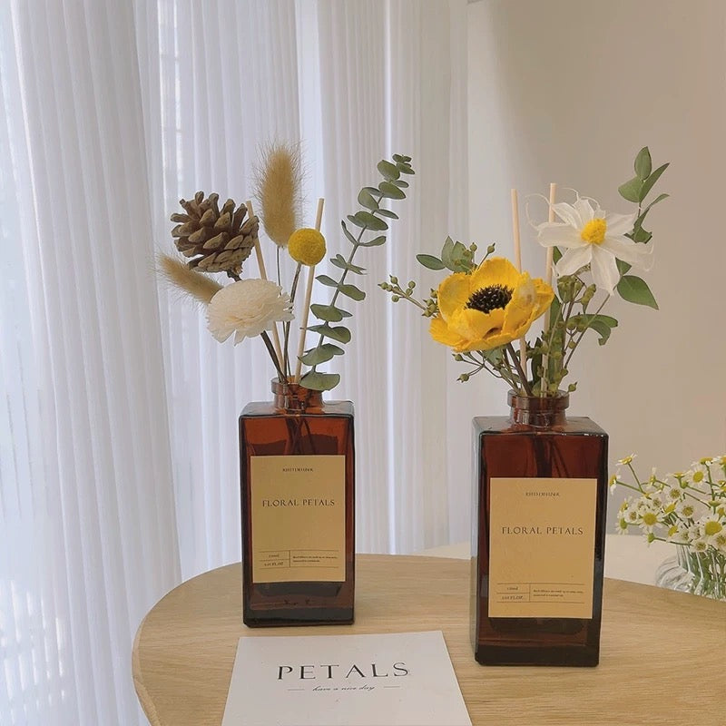 Two brown glass diffusers with floral arrangements on a wooden table.