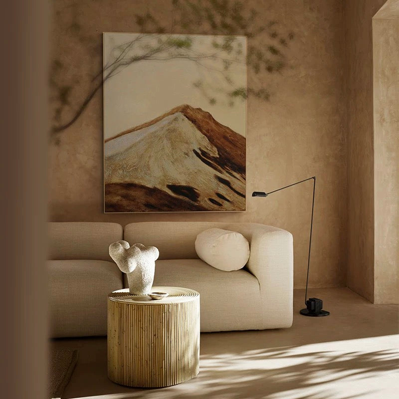Modern living room with a beige sofa, wooden side table, and abstract mountain painting.