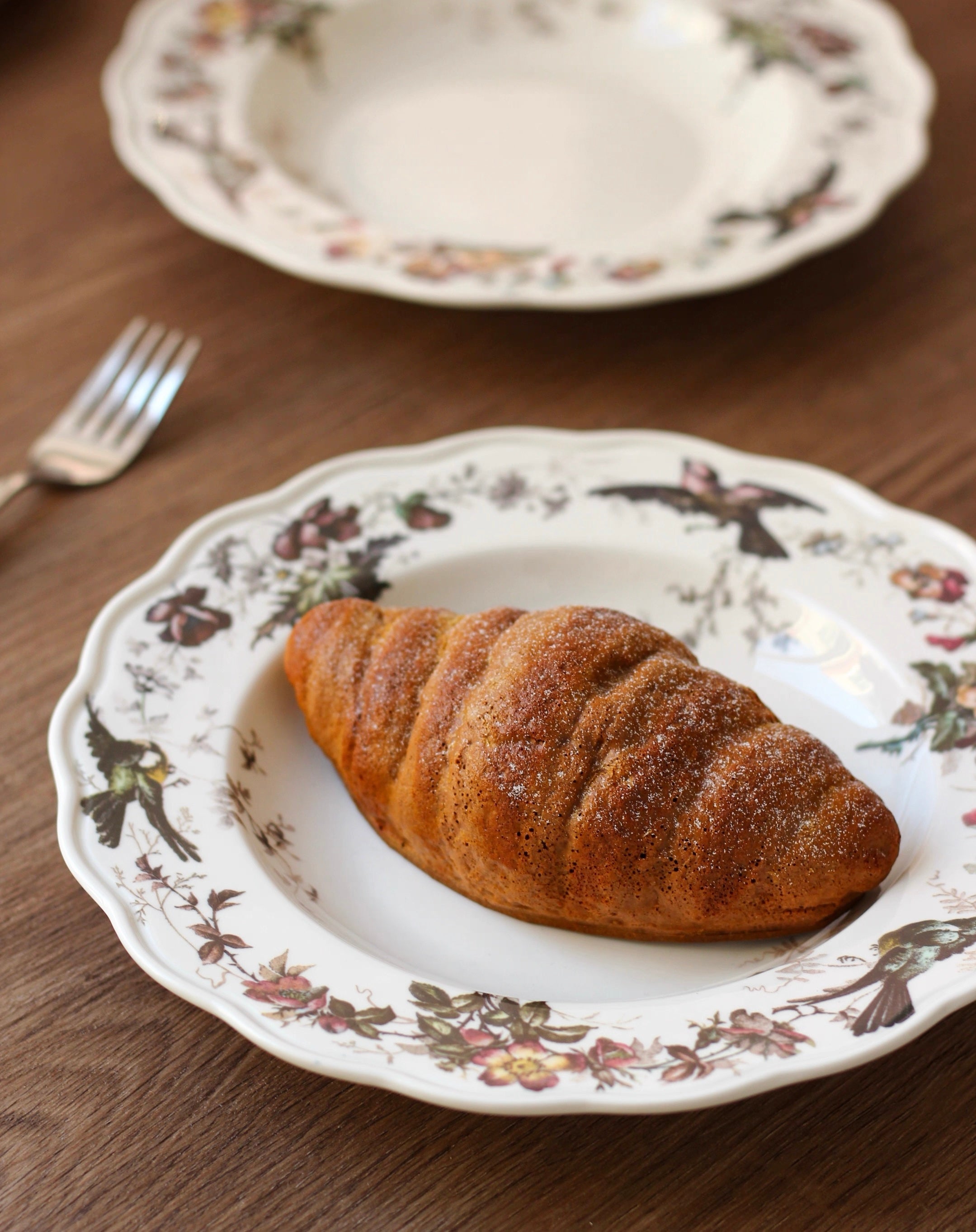 Croissant on a decorative plate with a floral pattern on a wooden table.