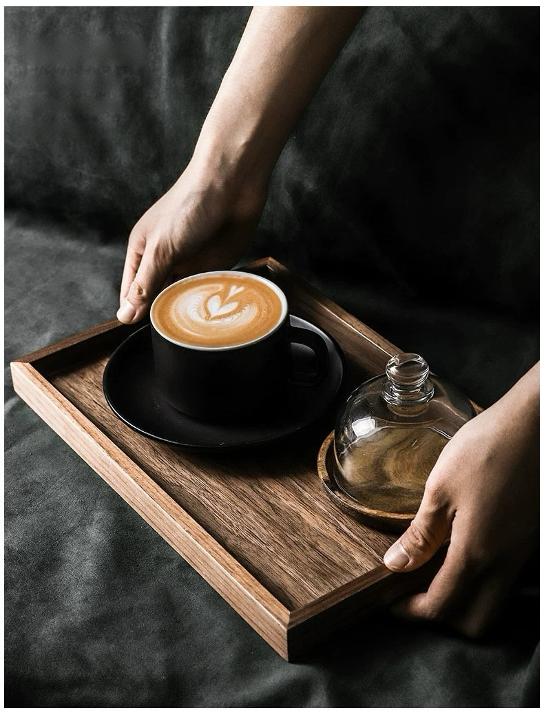 Person holding a wooden tray with a cup of coffee and a glass container on a dark surface