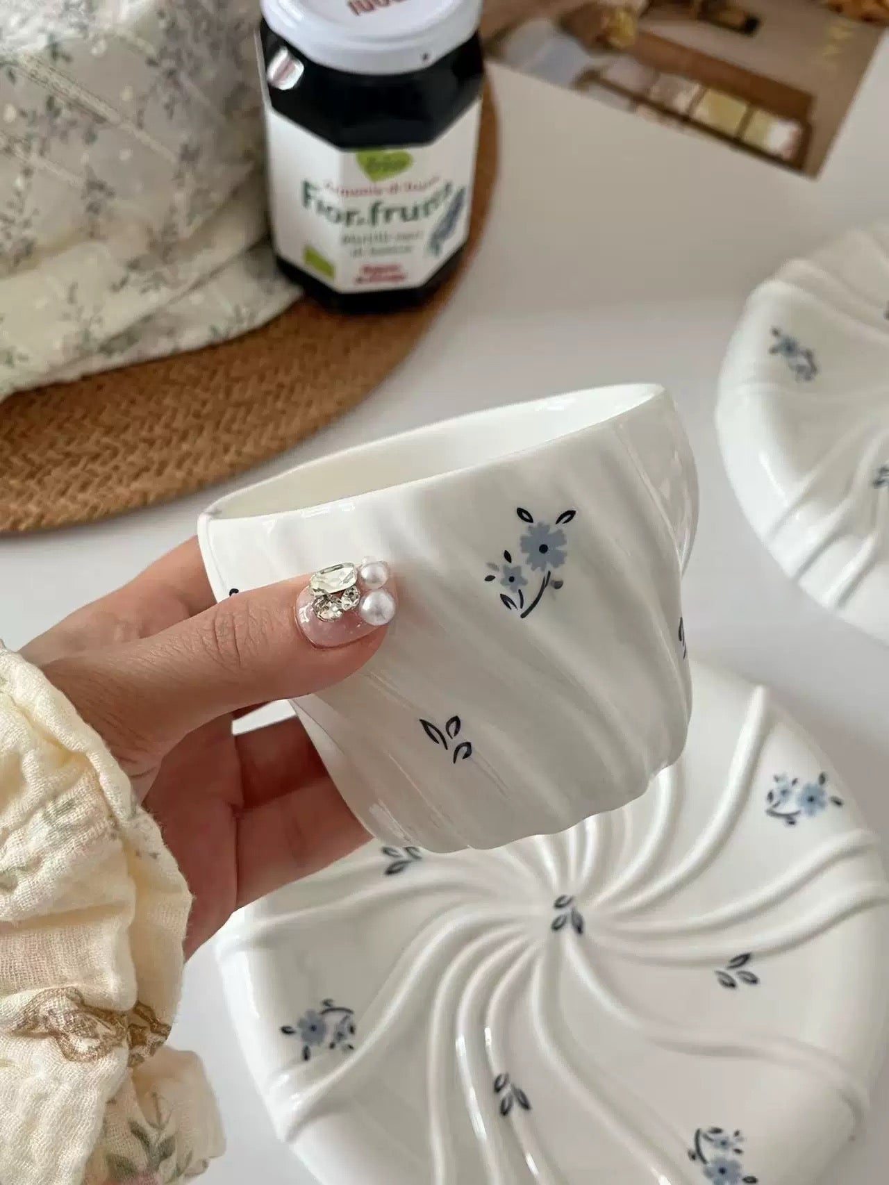Hand holding a white ceramic pot with floral designs on a blurred background