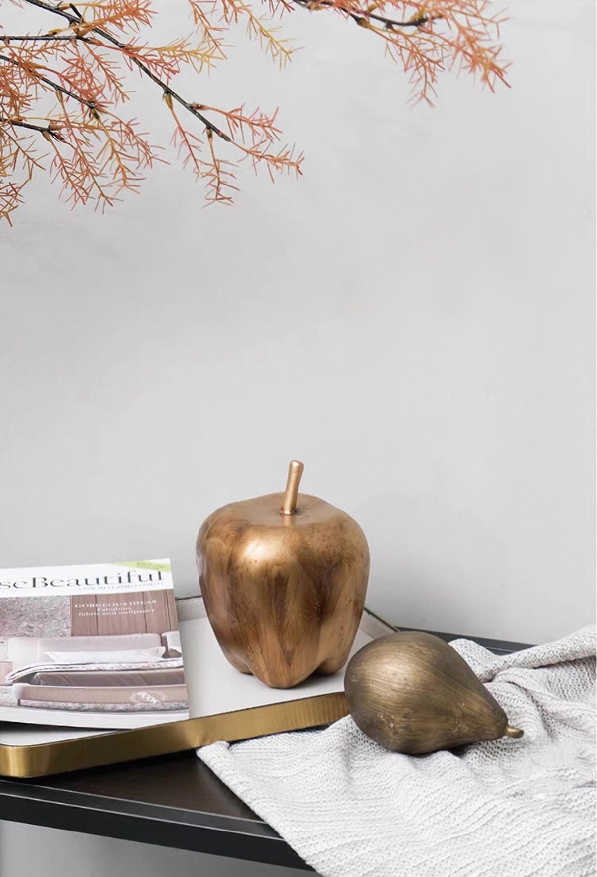 Bronze apple and pear on a table with a magazine and branch in the background