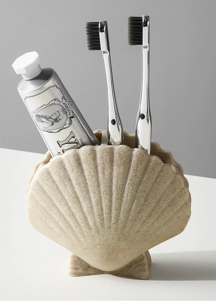 Shell-shaped holder with toothbrushes and toothpaste on a gray background