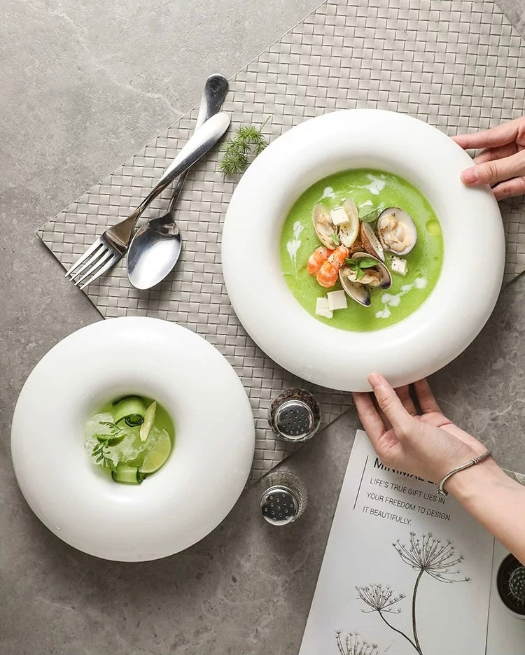 Two white bowls with green soup and seafood on a textured surface with cutlery.