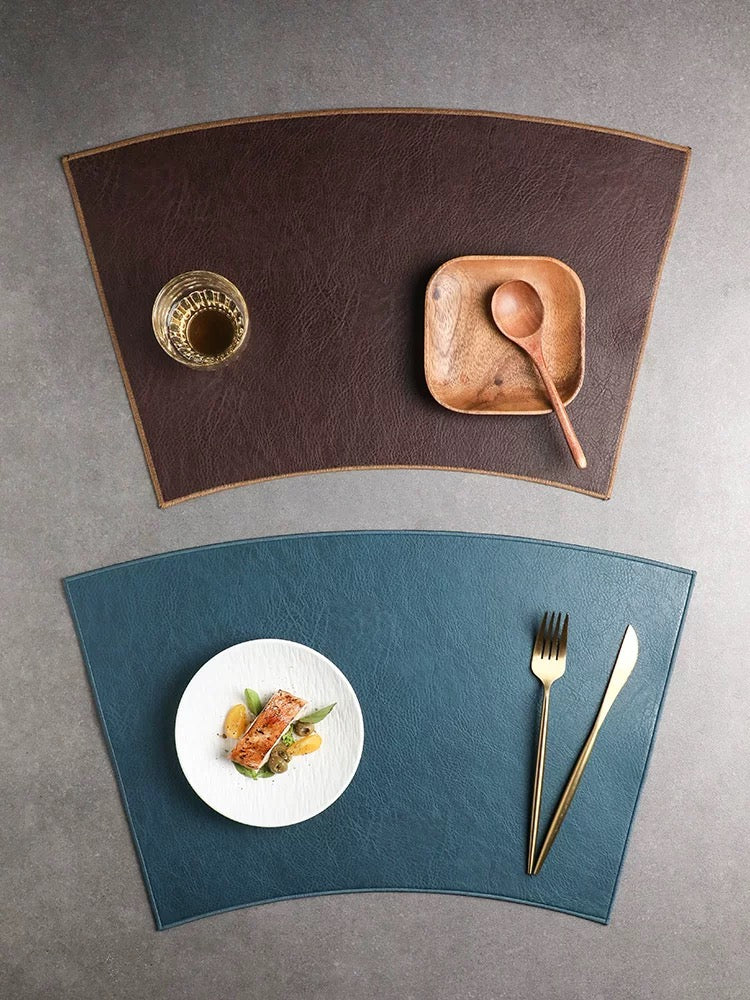 Two placemats, one brown and one blue, with a plate of food and cutlery on a gray surface.