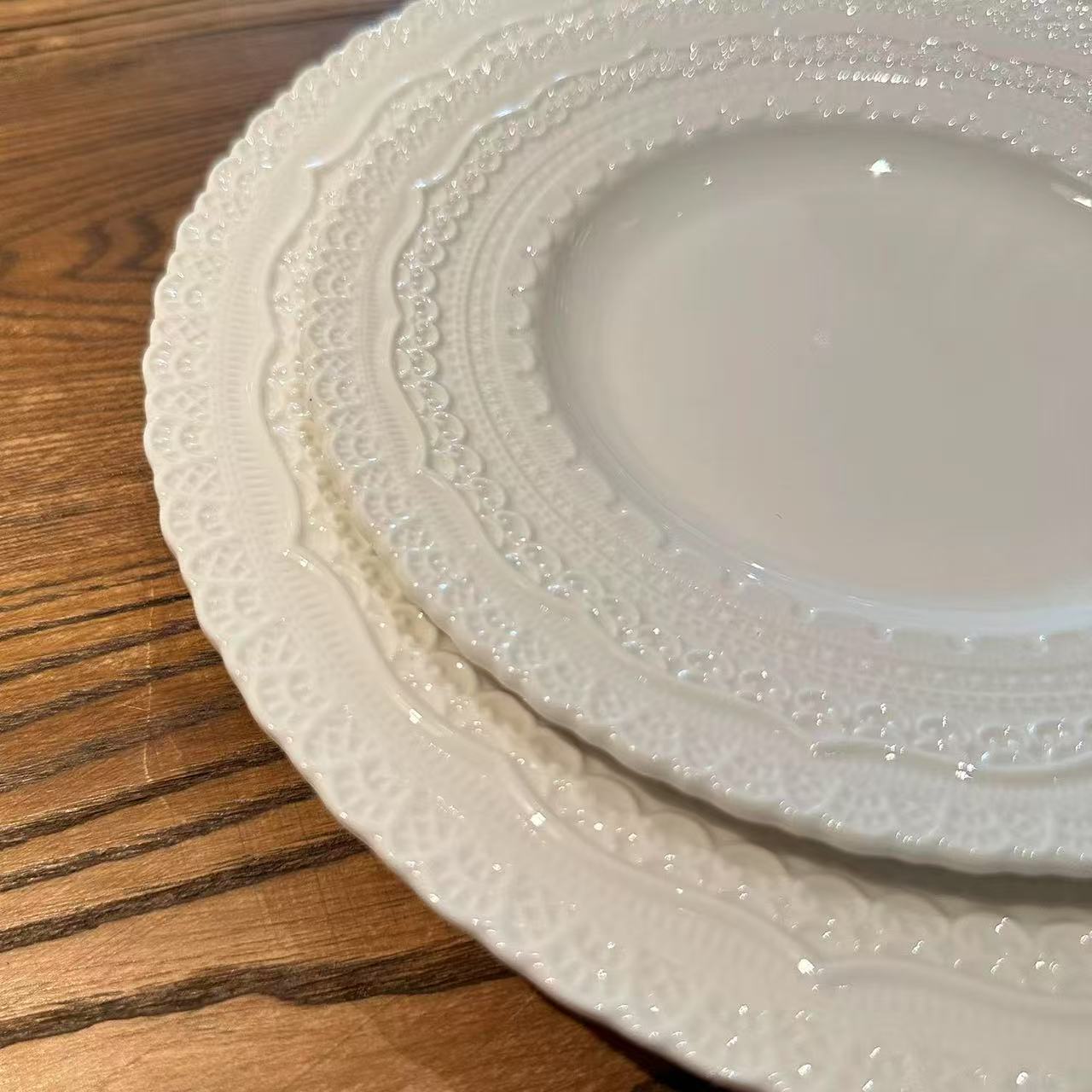 Stack of white ceramic plates with textured rim on a wooden surface